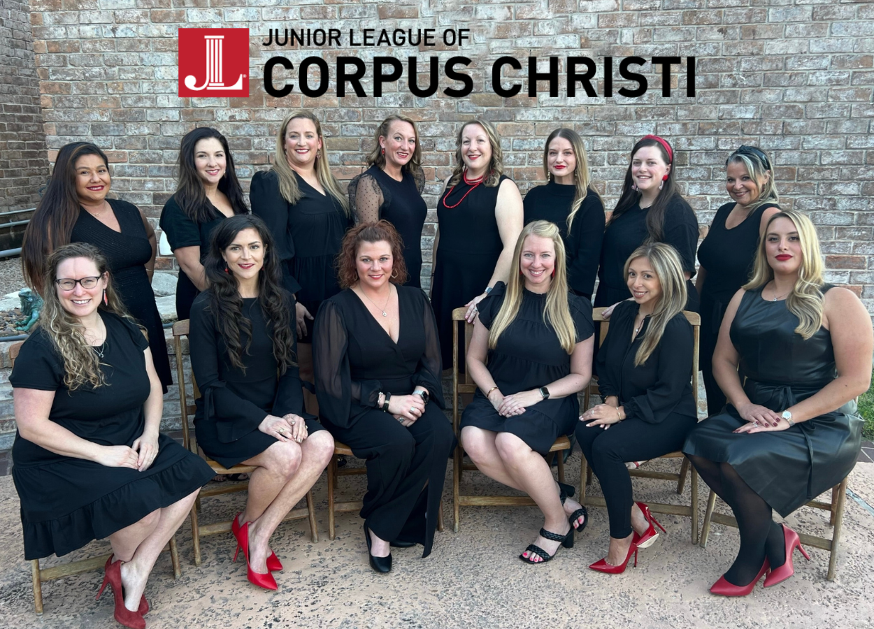 Photo of fourteen women, seven seated and seven standing. All women serve on the Board of Directors for the Junior League of Corpus Christi. They are all wearing black with red accessories.